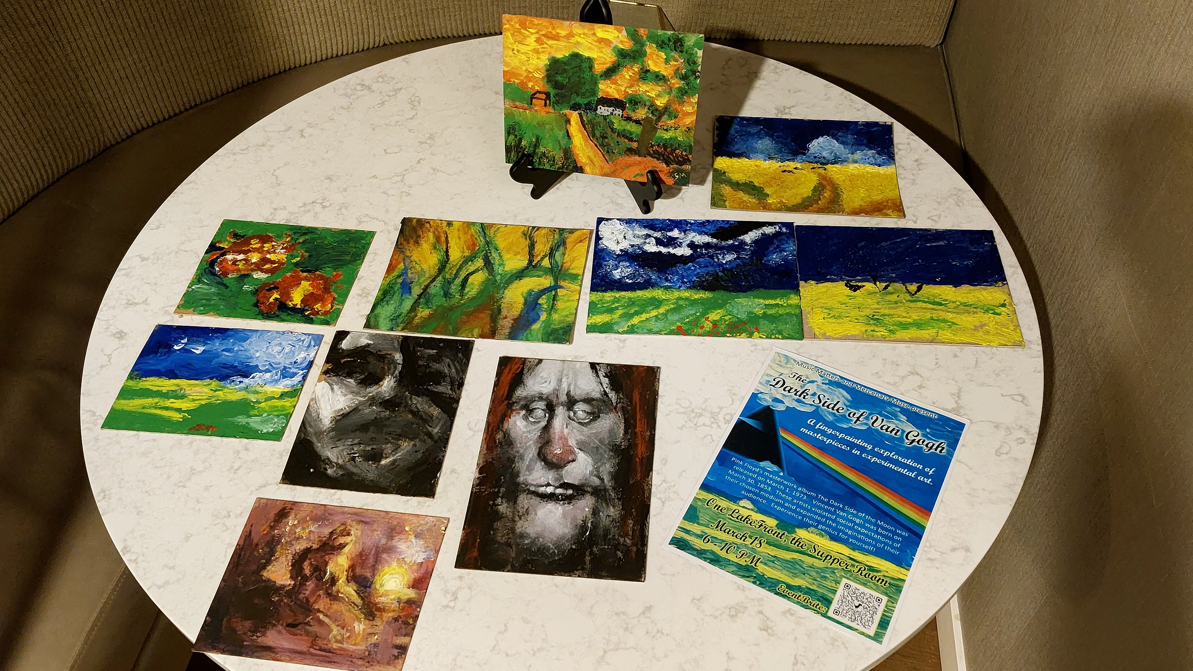 Collection of participant paintings assembled on a tabletop with event promotional card